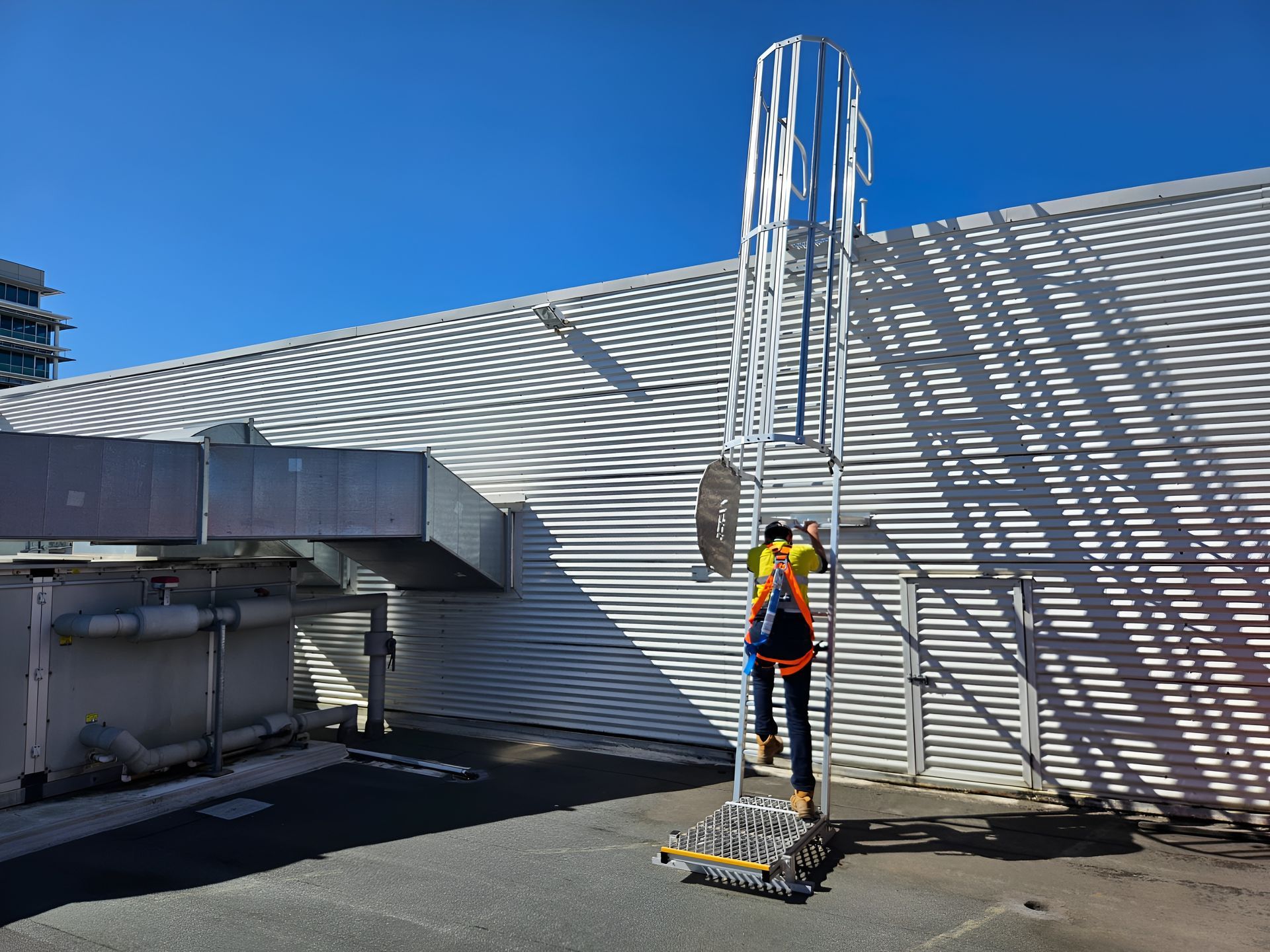 Worker in Safety Harness Climbing a Tall Ladder on a Rooftop — Australian Asset Compliance in Gladstone, QLD