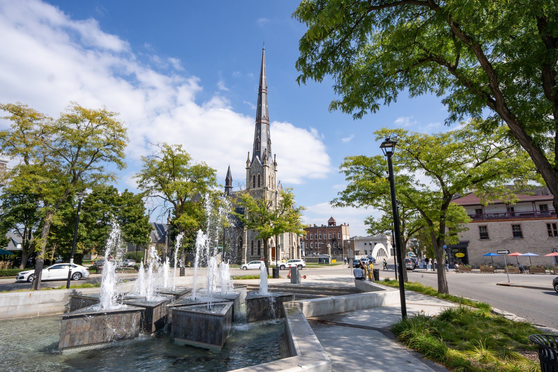 Fountain in a town square with a tall church in the background under a bright blue sky.