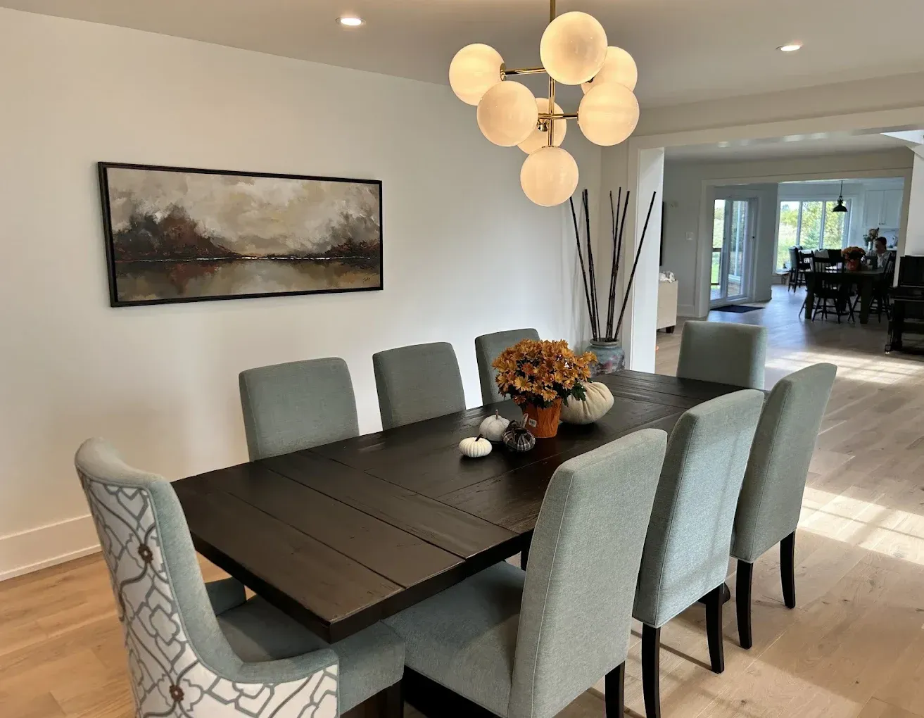 Dining room with a dark table, eight gray chairs, art, and a modern light fixture.