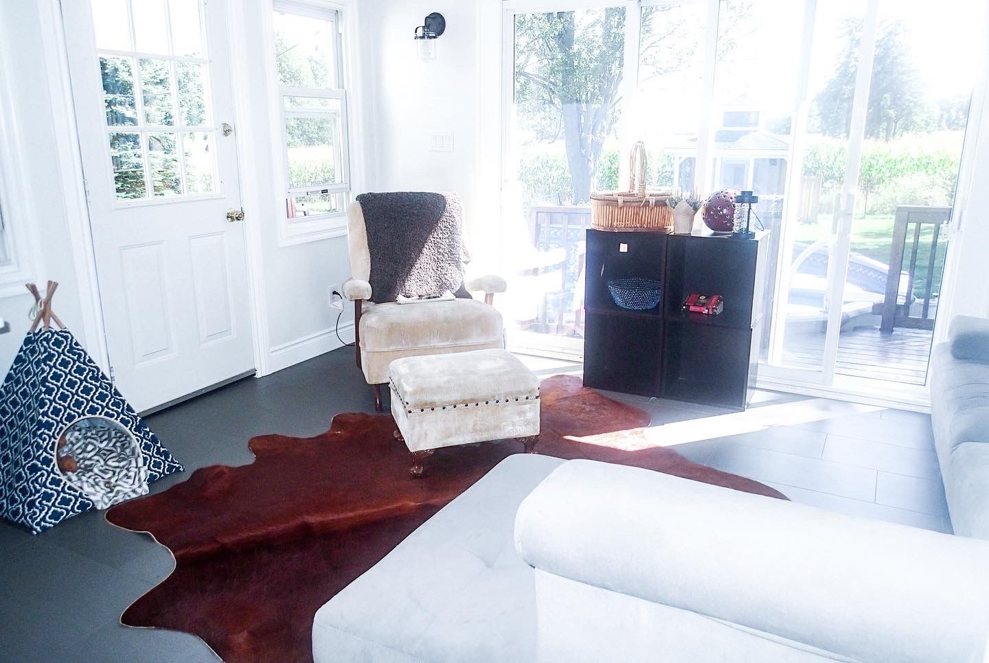 Bright sunroom with white furniture, dark rug, and a child's play tent.