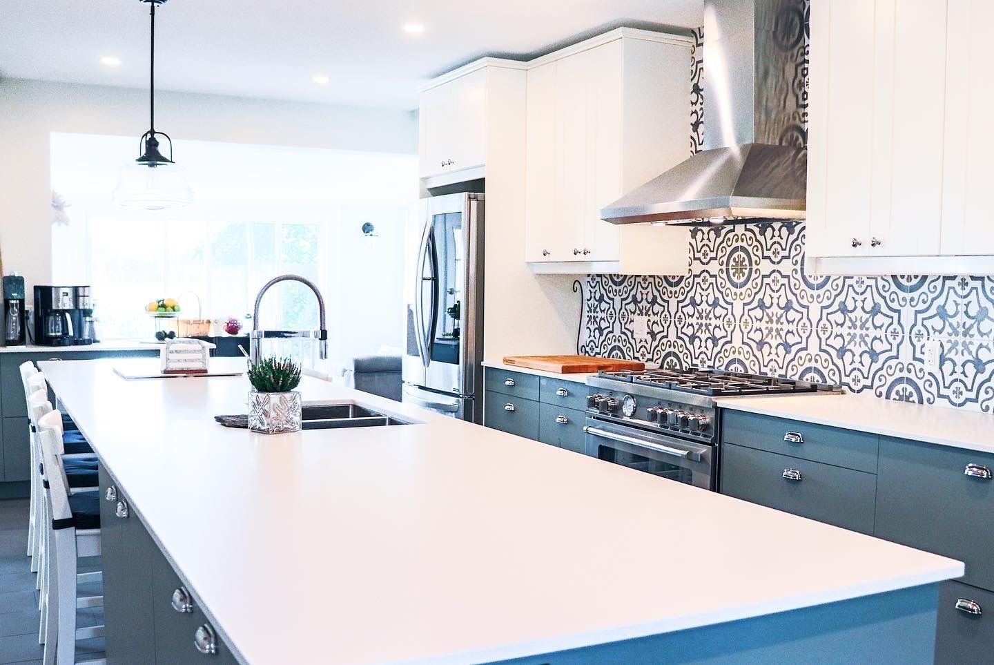 Modern kitchen with white island, gray cabinets, blue accents, and decorative tile backsplash.