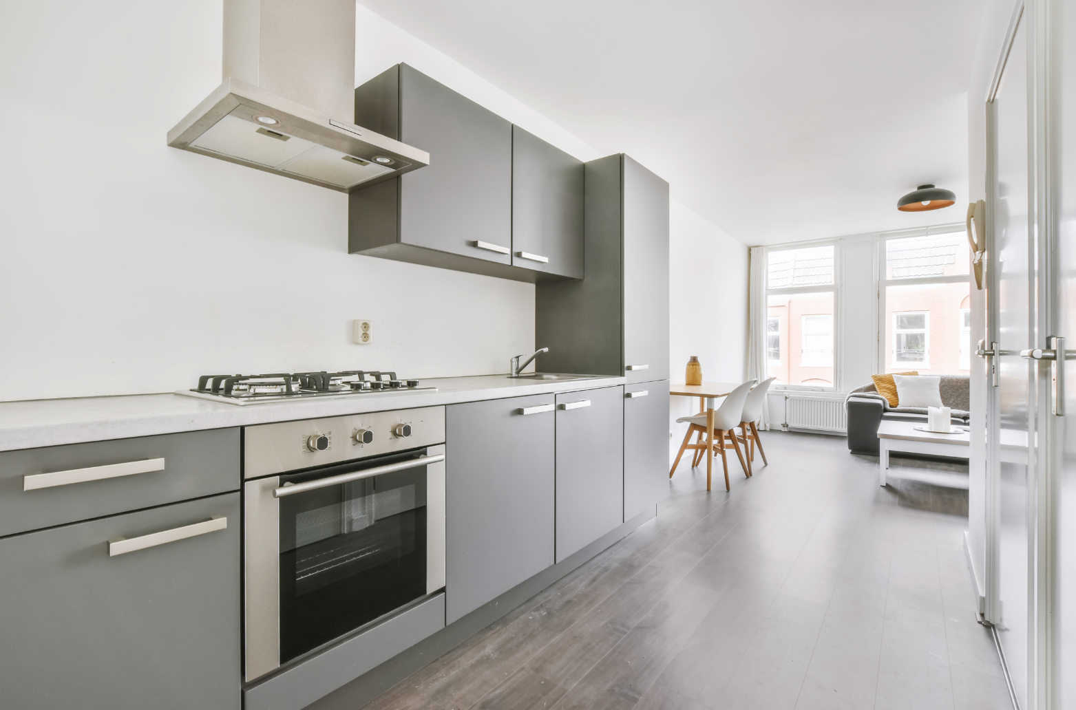 Modern gray kitchen with stove, oven, and cabinetry; connected to a living area with furniture.