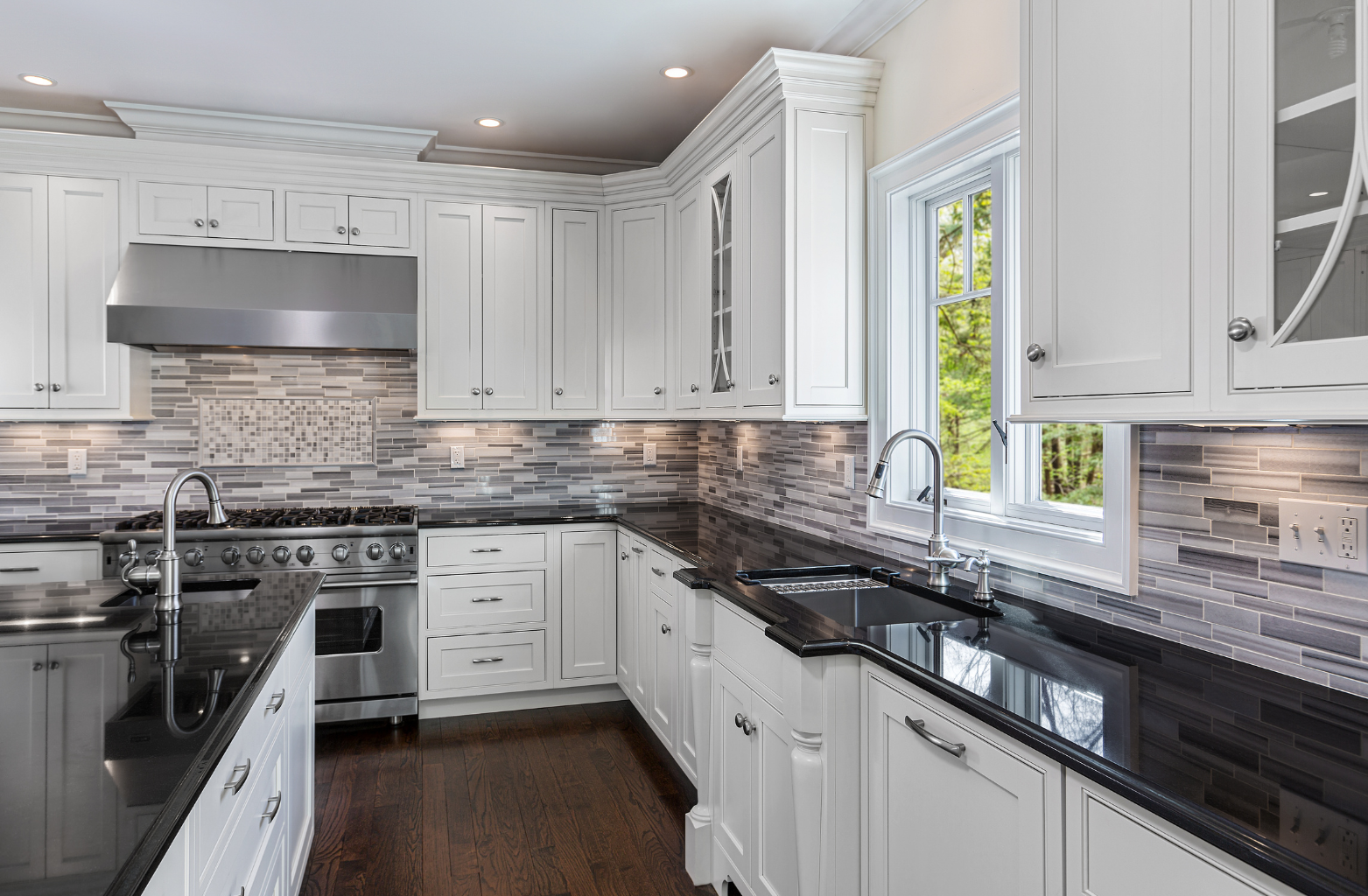 White kitchen with black countertops, stainless steel appliances, and a window.