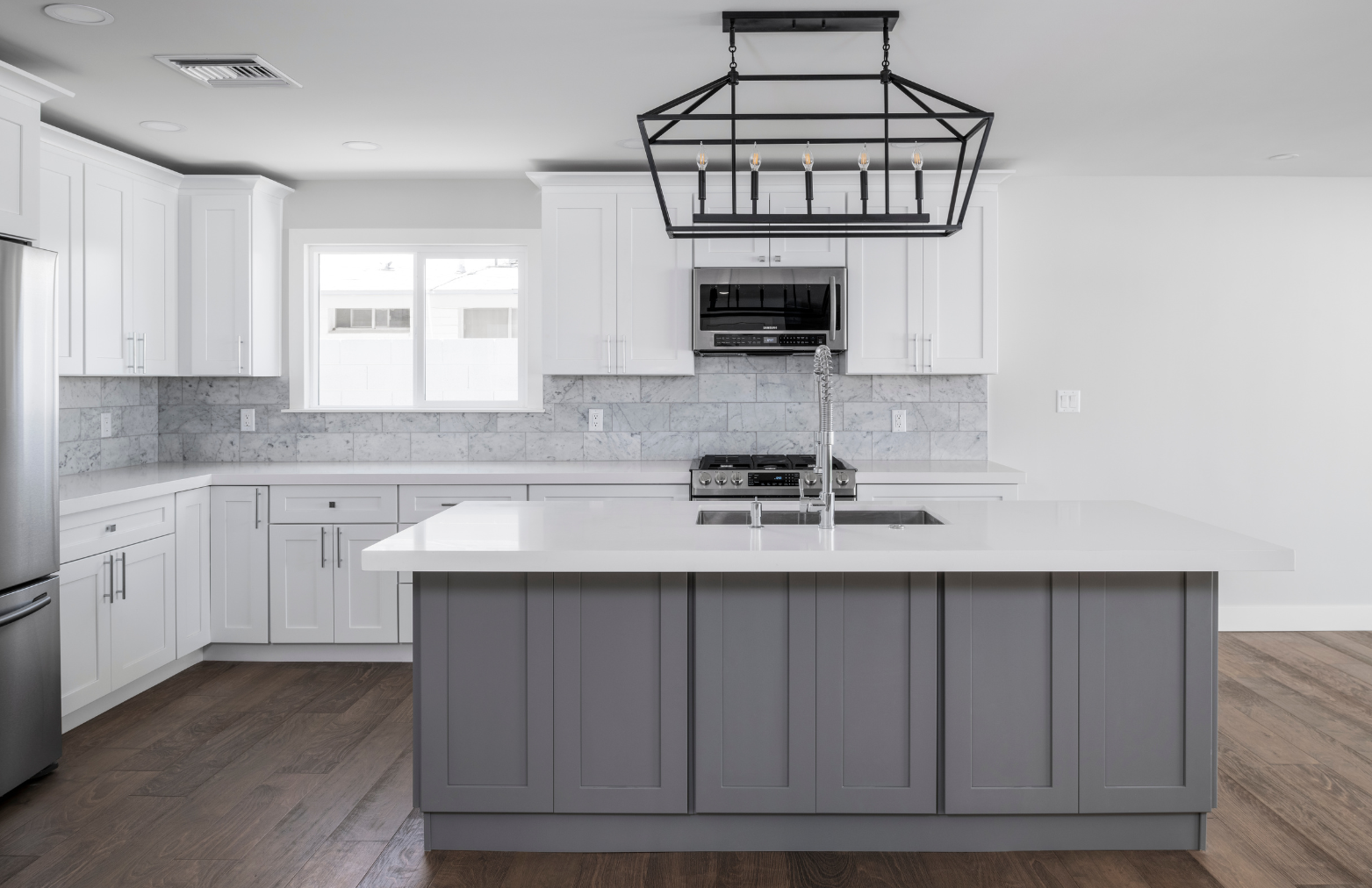 Modern kitchen with white and gray cabinets, stainless steel appliances, and a large island.