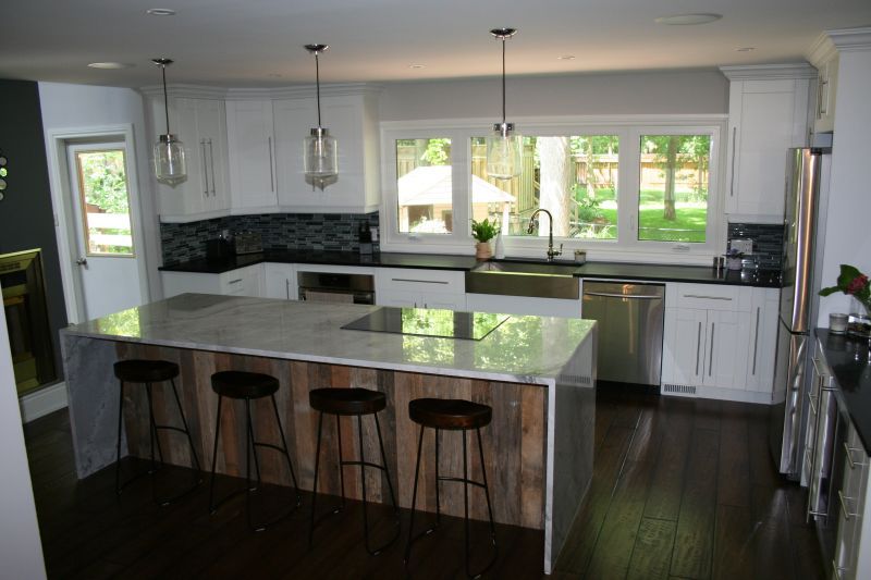 Modern kitchen with white cabinets, wood island, dark countertops, stainless steel appliances.