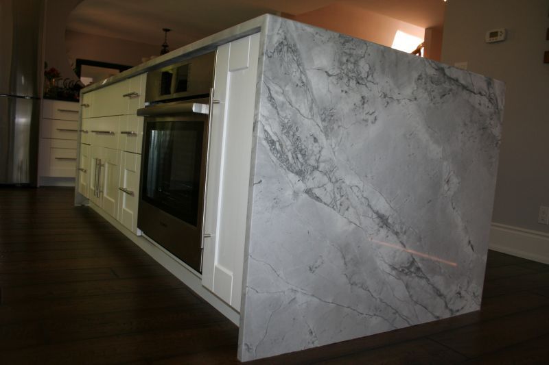 Kitchen island with marble countertop, oven, and white cabinets.