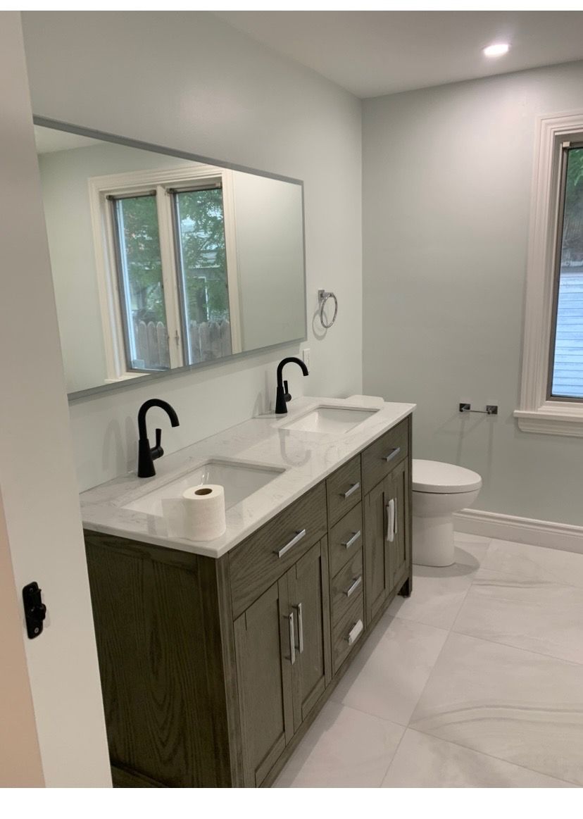 Bathroom with gray double vanity, marble countertop, black faucets, large mirror, and toilet.