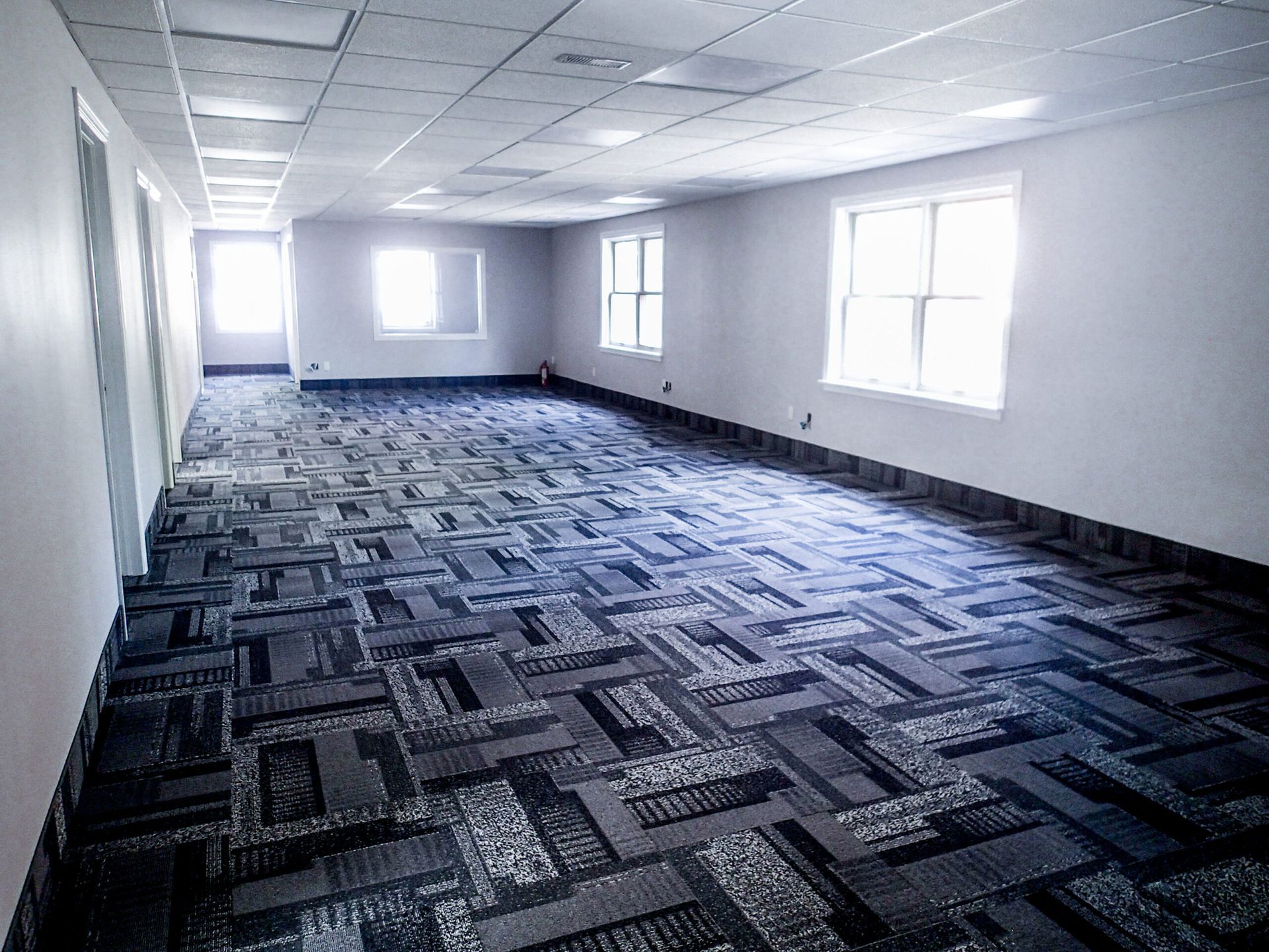 Empty office space with patterned carpet, windows, and white walls.