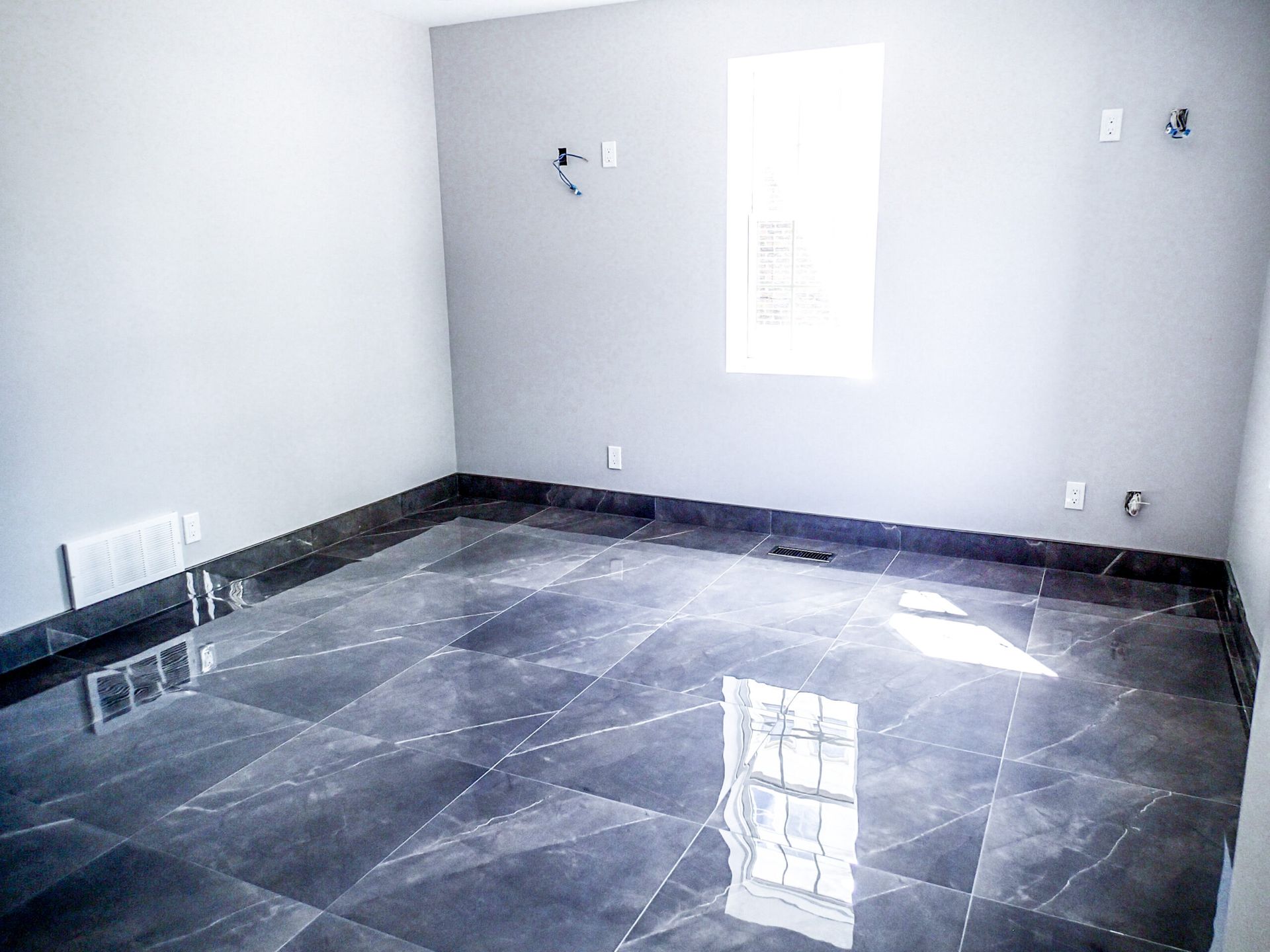 Empty room with gray walls, a bright window, and shiny dark tile floor.