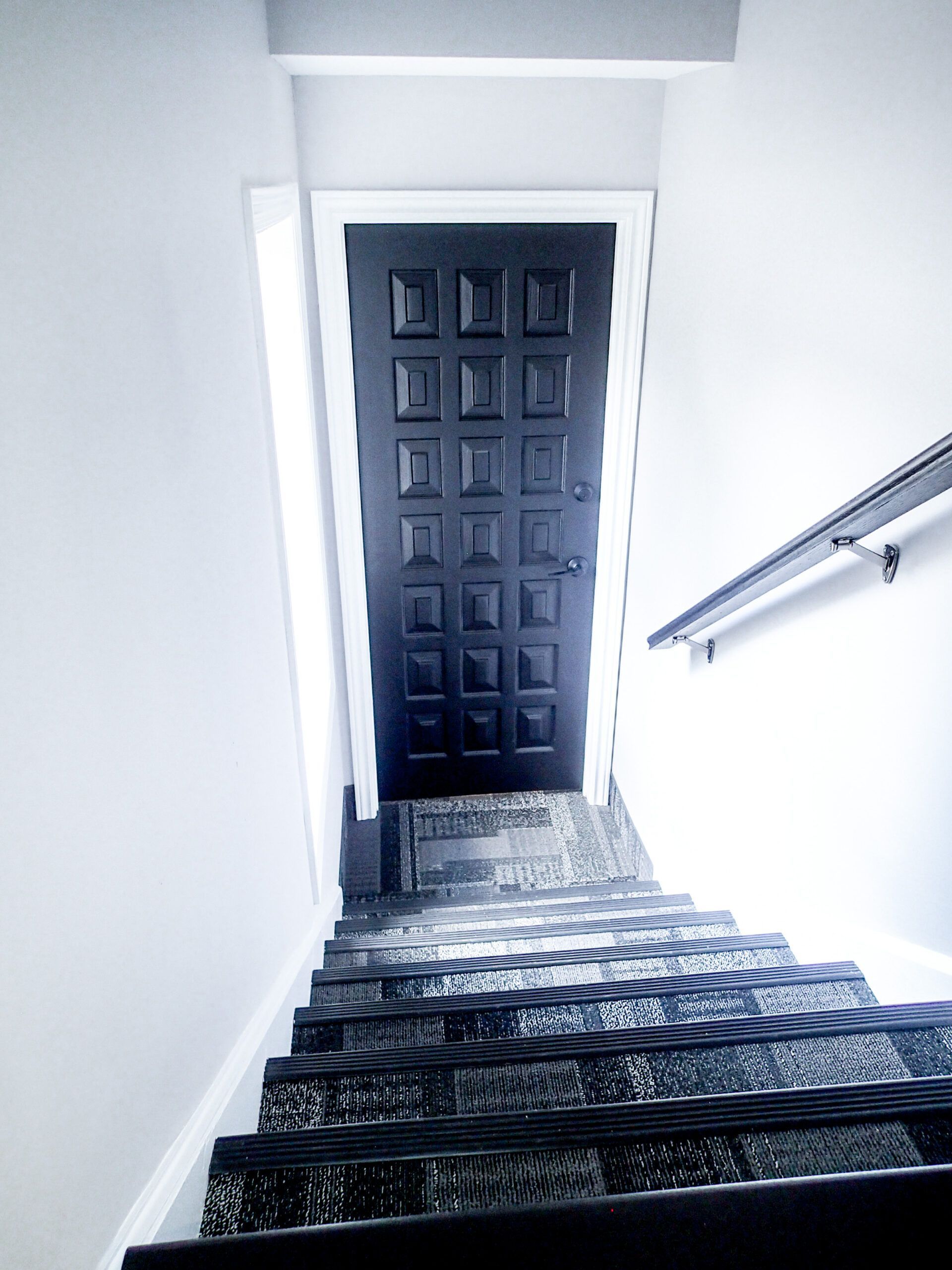Stairwell leading up to a dark door. Stairs have patterned carpet. White walls.