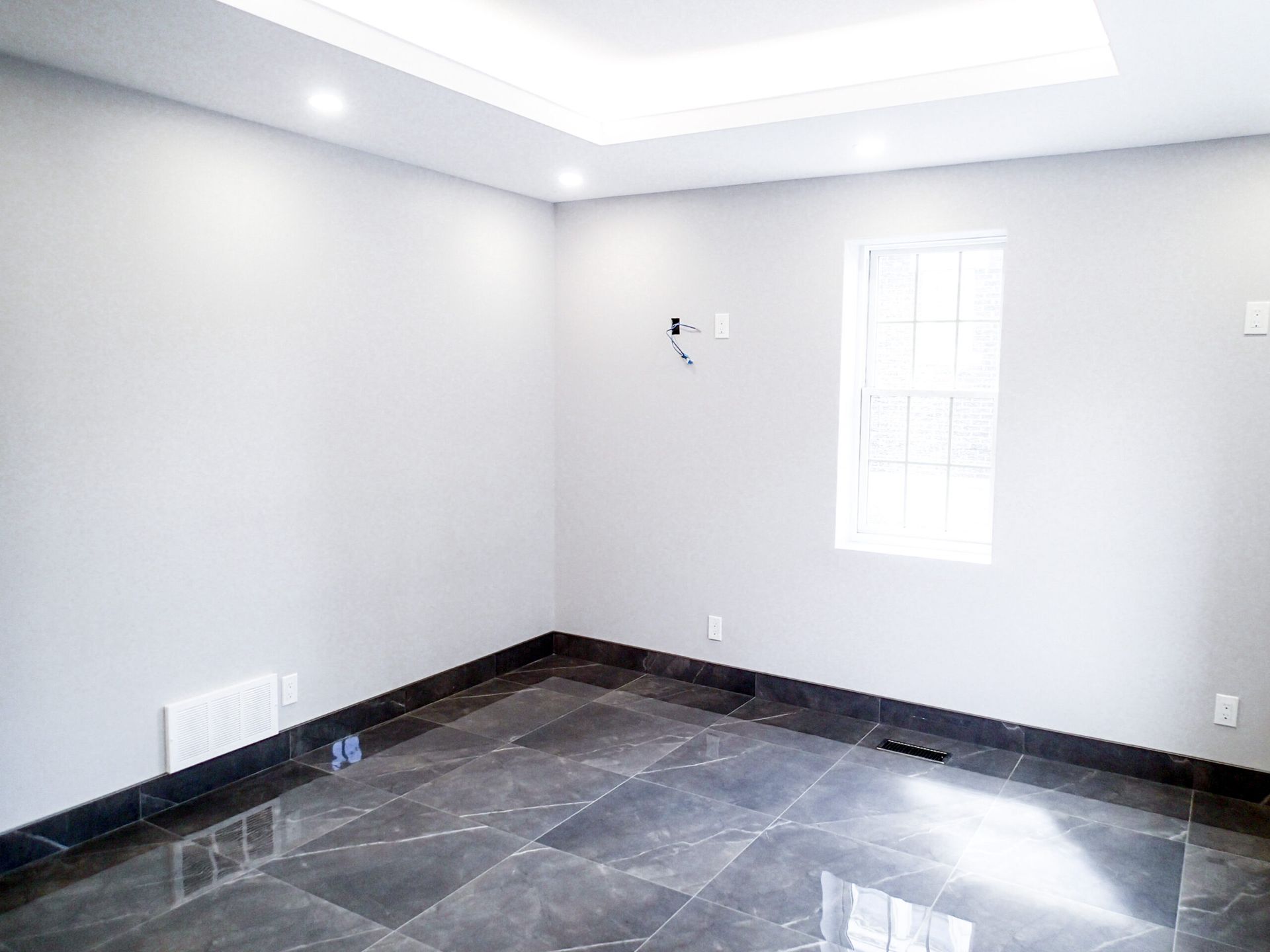 Empty room with gray walls, dark tiled floor, and a window.