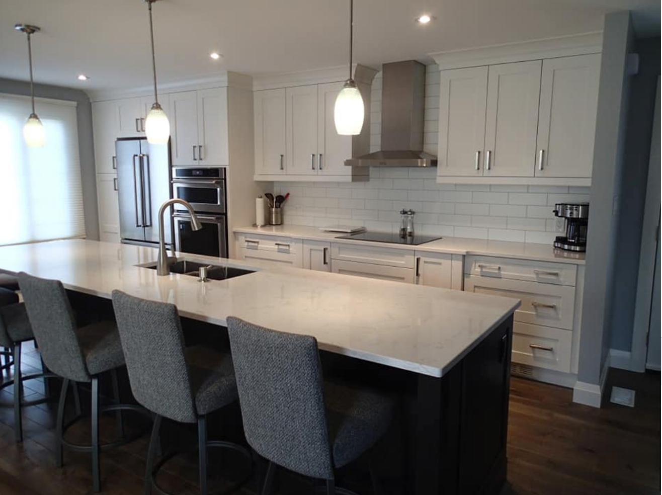 Modern kitchen with white cabinets, large island with seating, stainless steel appliances, and wooden floor.