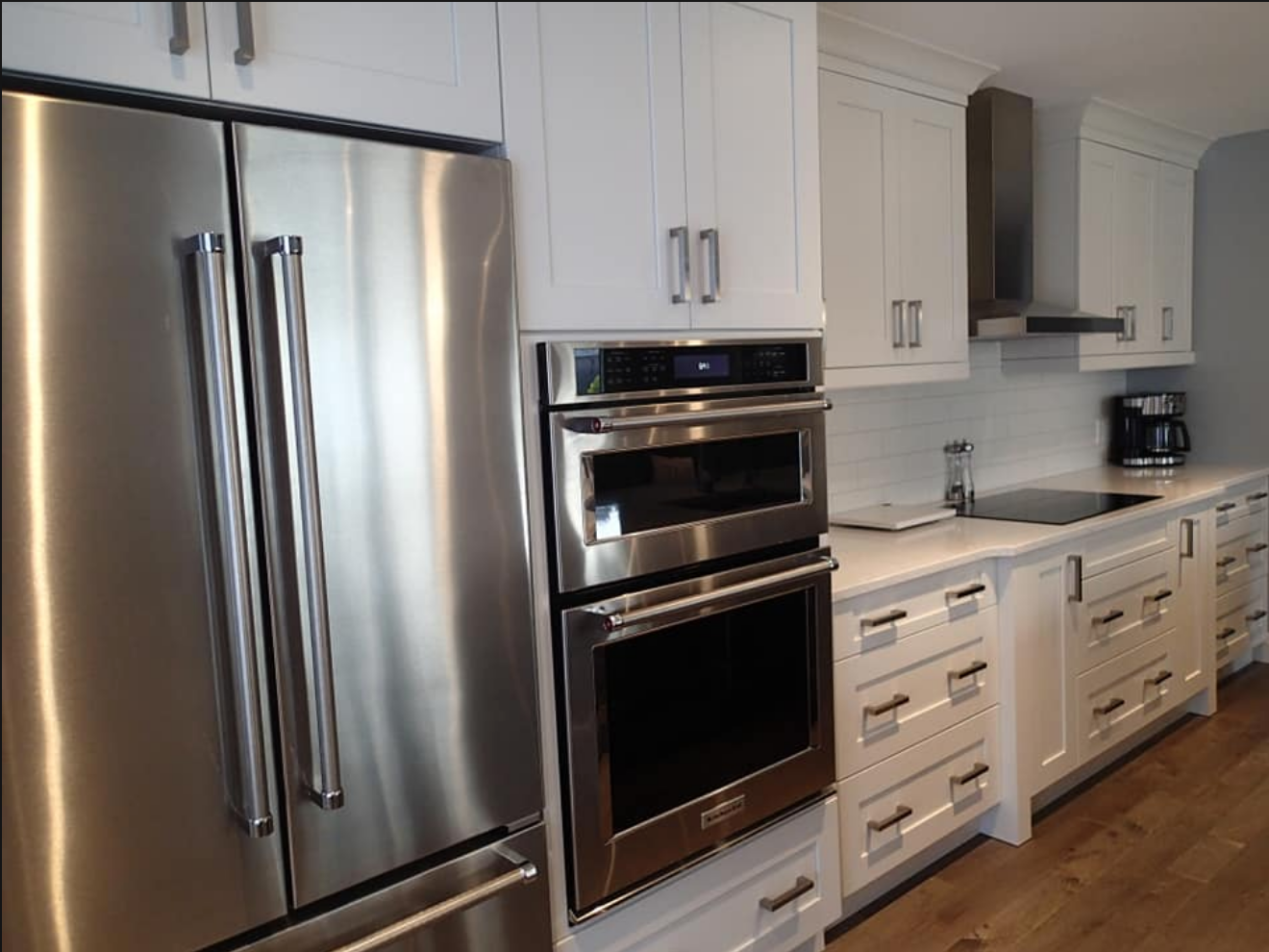 Stainless steel refrigerator and double oven in white modern kitchen.