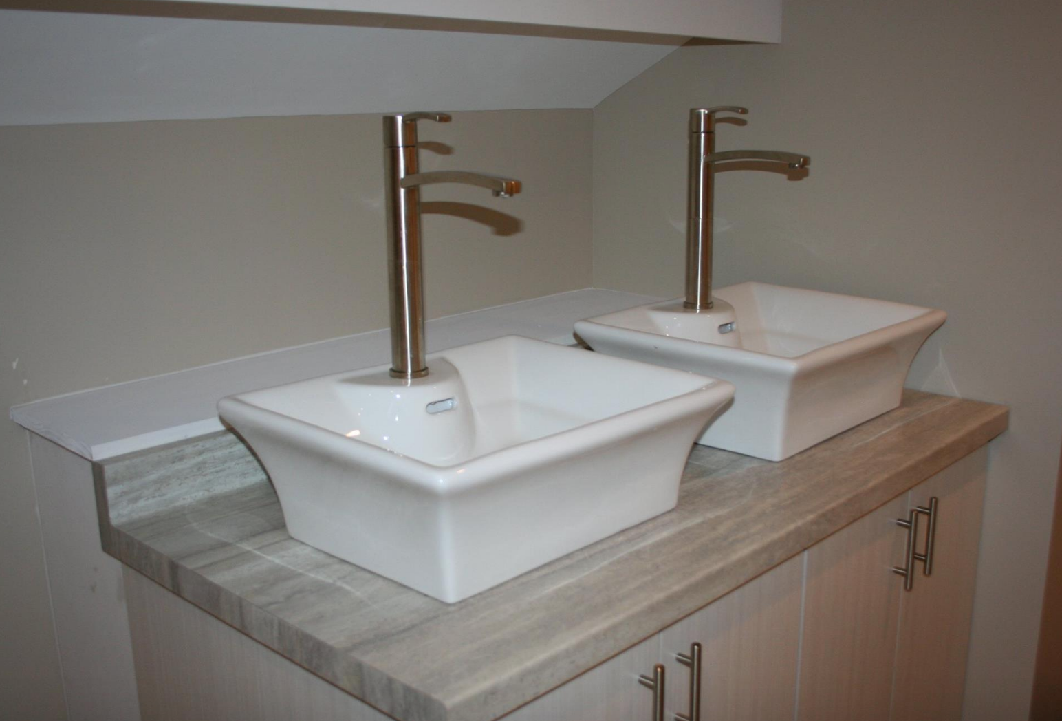 Two white rectangular sinks on a counter with silver faucets, cabinets below.