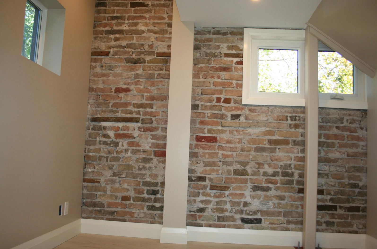 Brick interior wall with two windows, painted white trim, and neutral paint on adjacent walls.