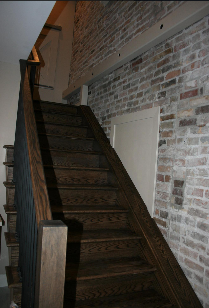 Wooden staircase with dark treads and brick wall. Railing on left. Door visible.