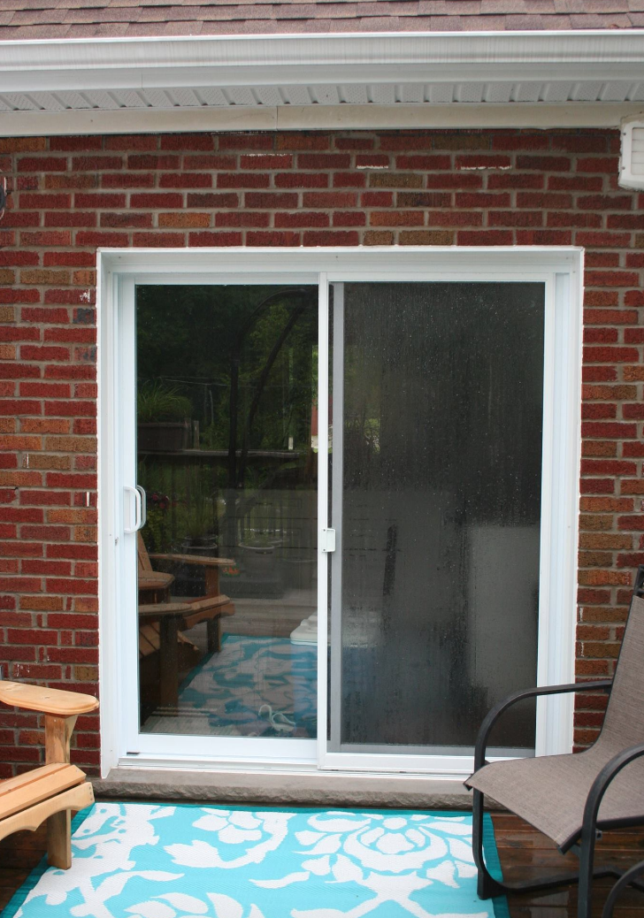 White-framed sliding glass door on a brick wall, leading to a patio with blue rug and outdoor seating.