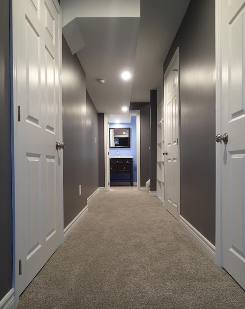 Long hallway with gray walls, white doors, and a light gray carpet leading to a bathroom.