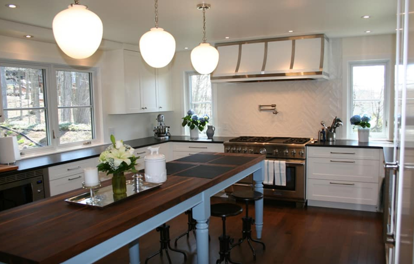 Modern white kitchen with dark wood island, stainless steel appliances, and pendant lights.