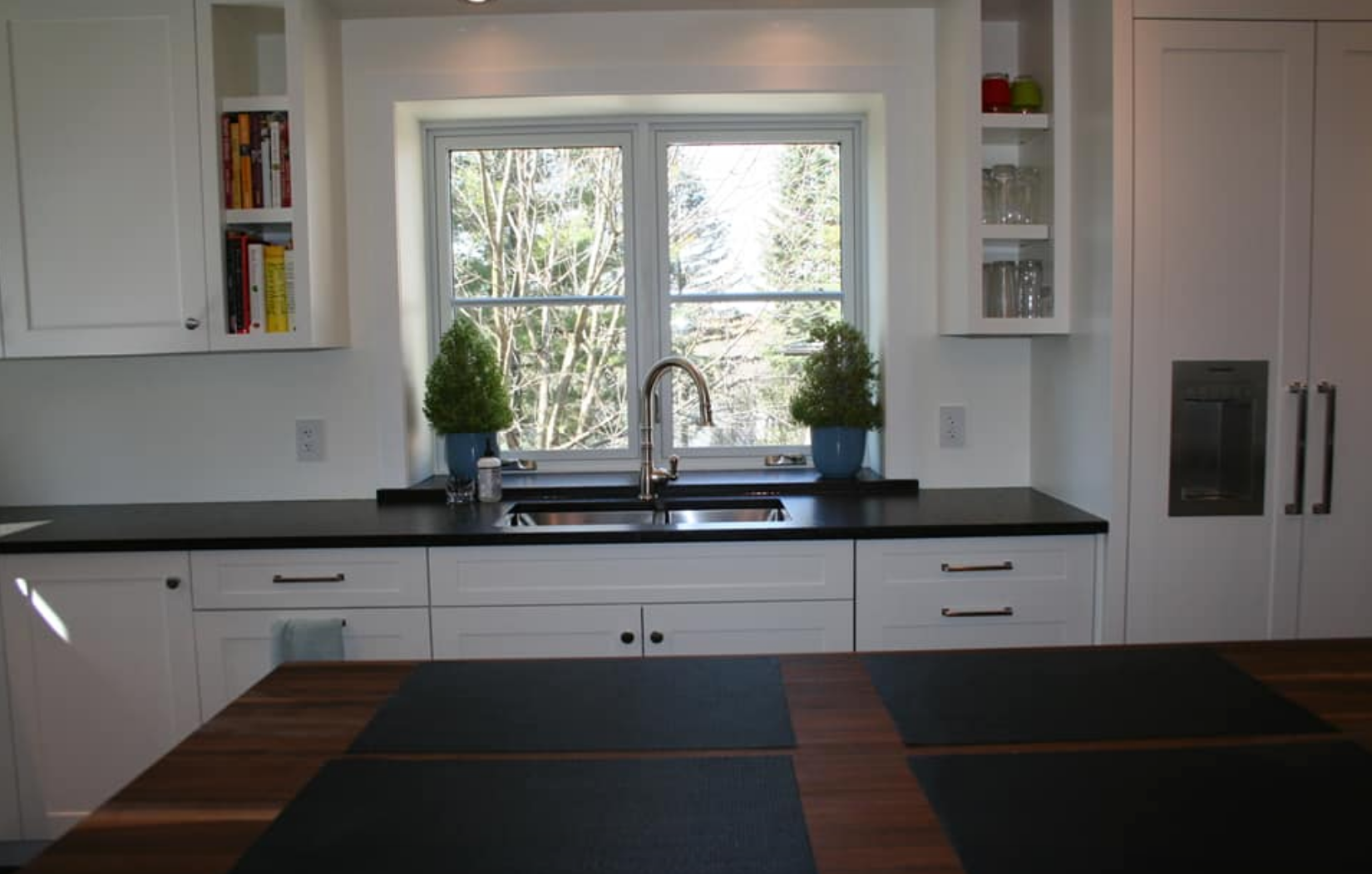 White kitchen with black countertops, sink under window, and wooden island.