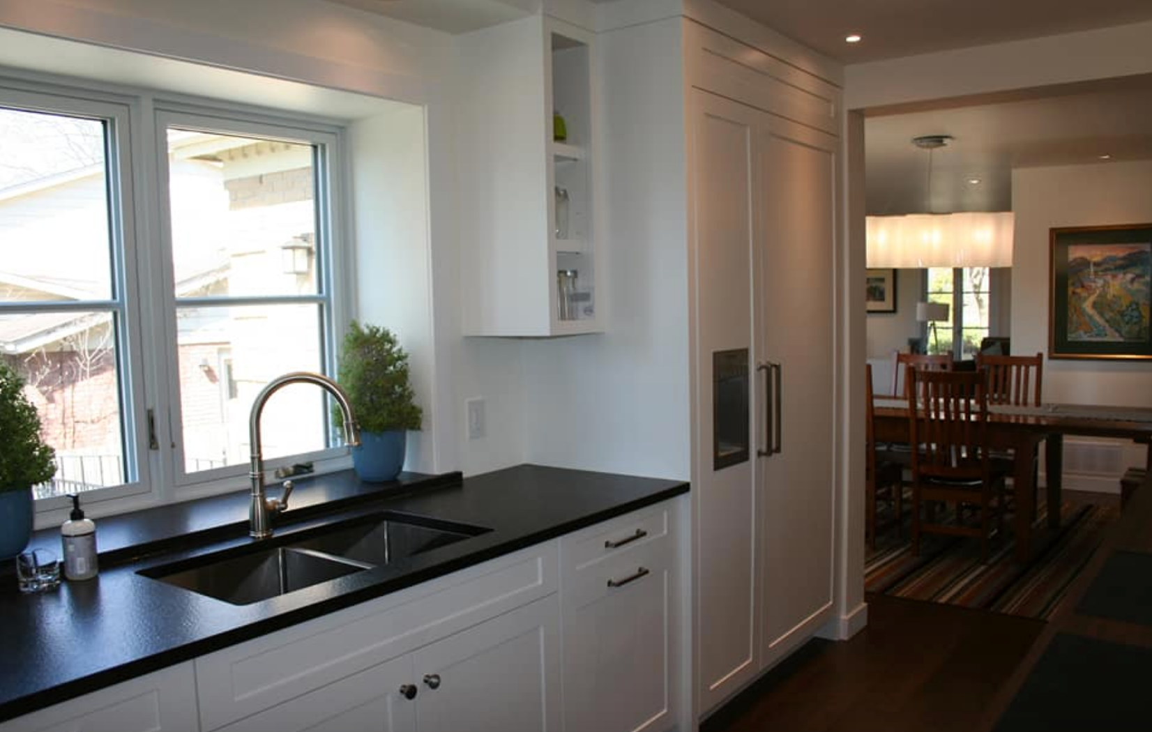 White kitchen with black countertops, stainless steel sink, and view into a dining room.