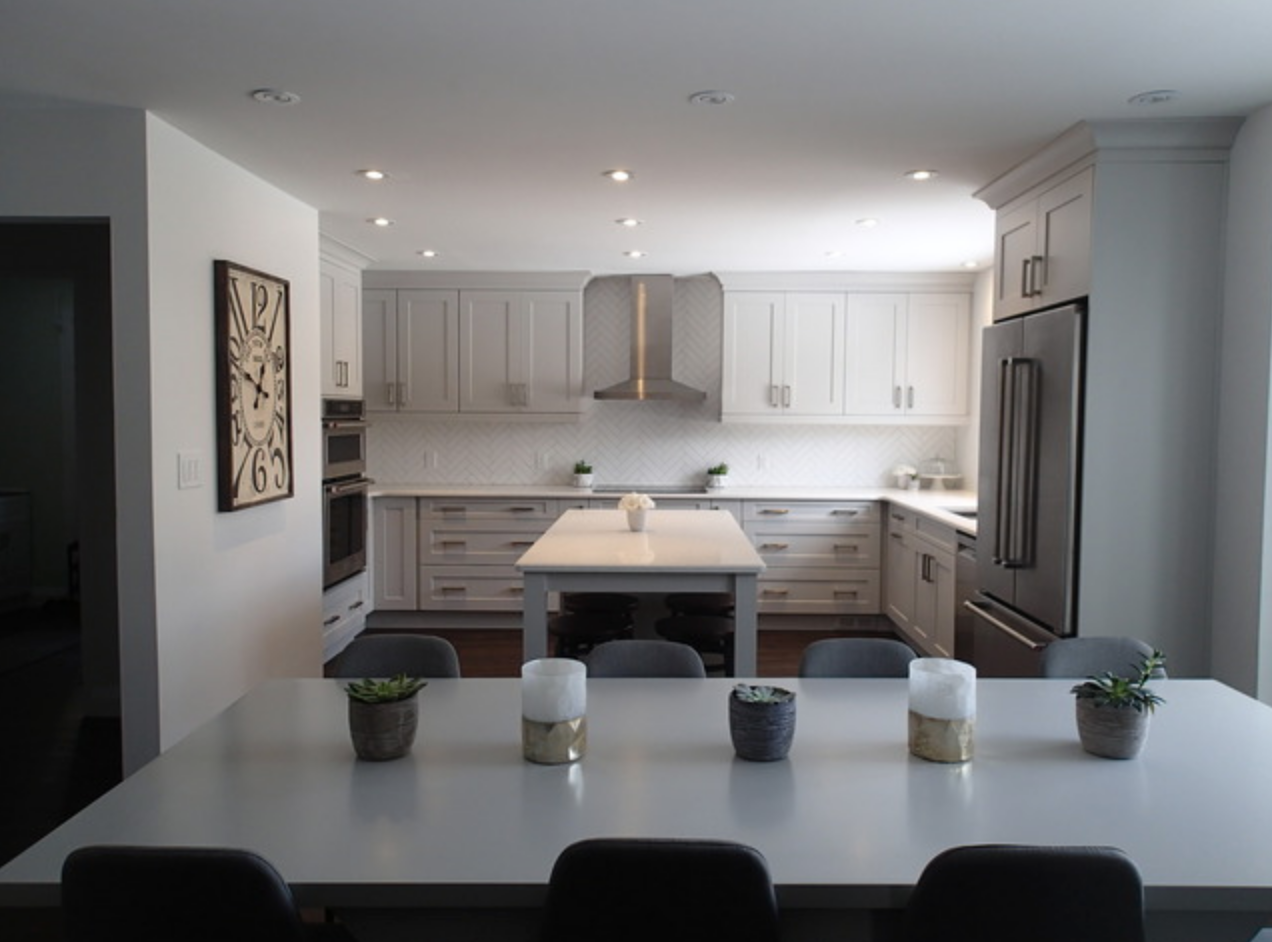 Modern kitchen with white cabinets, island, and stainless steel appliances. Long dining table with chairs in front.