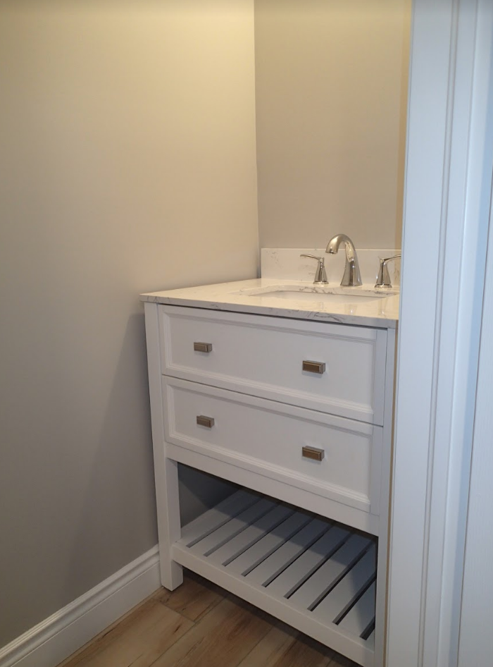 White bathroom vanity with drawers and a shelf, against a beige wall.