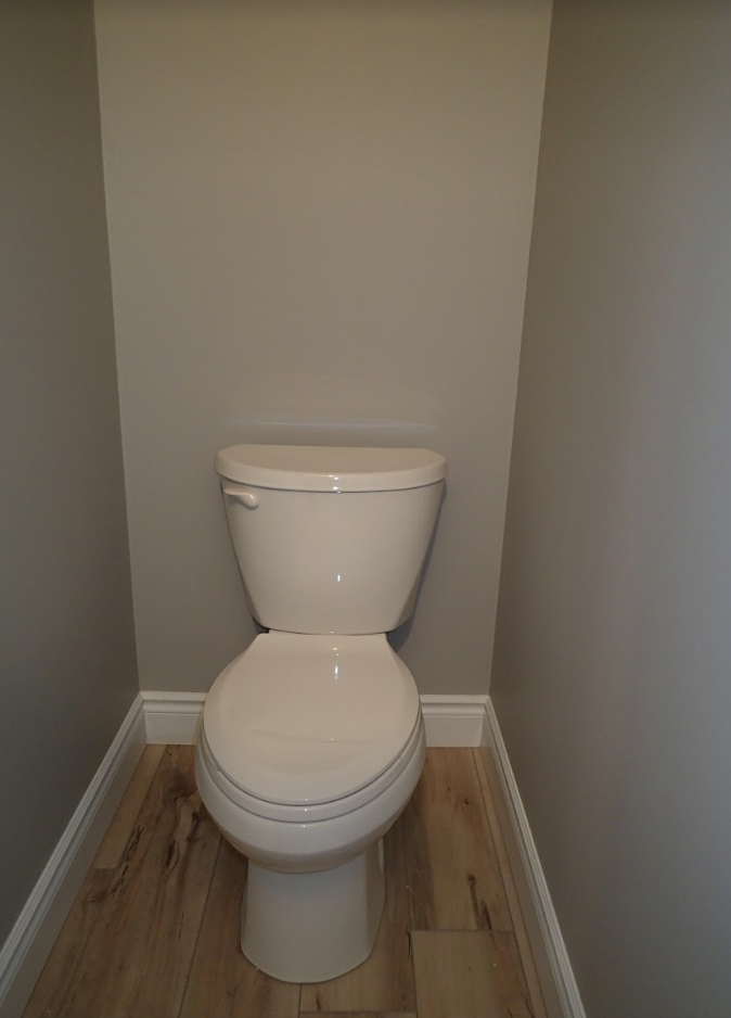 Toilet in a small bathroom alcove with light wood-look flooring and gray walls.