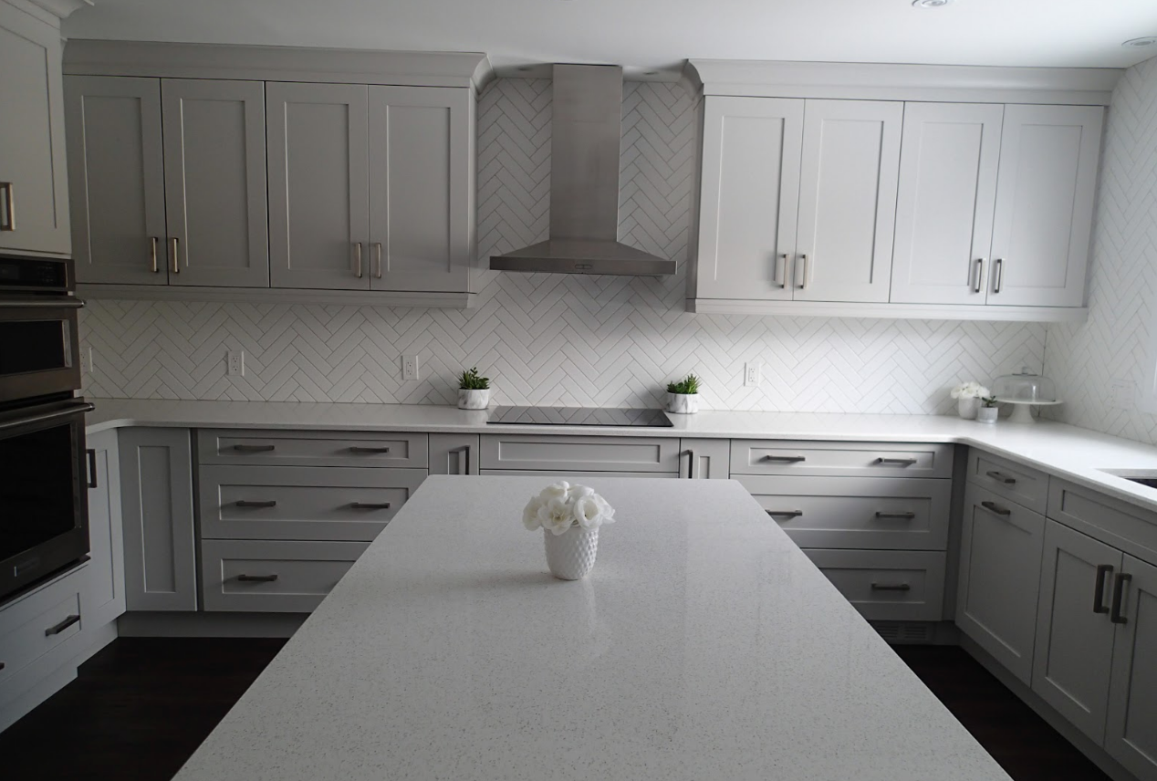 Light gray kitchen with white countertops, cabinets, and island; stainless steel range hood.