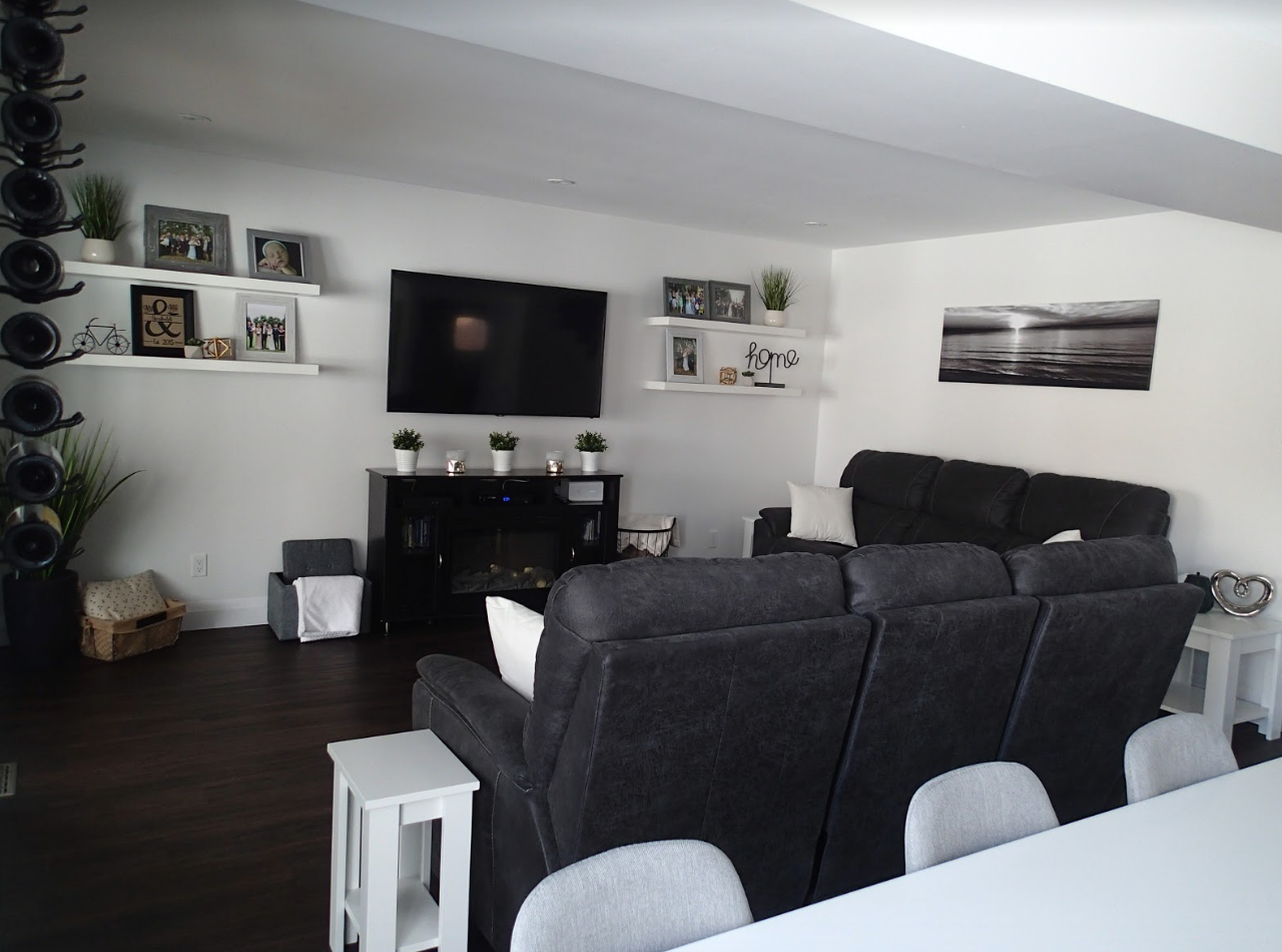 Living room with dark gray sofas, white walls, a black TV, and shelves with decor.