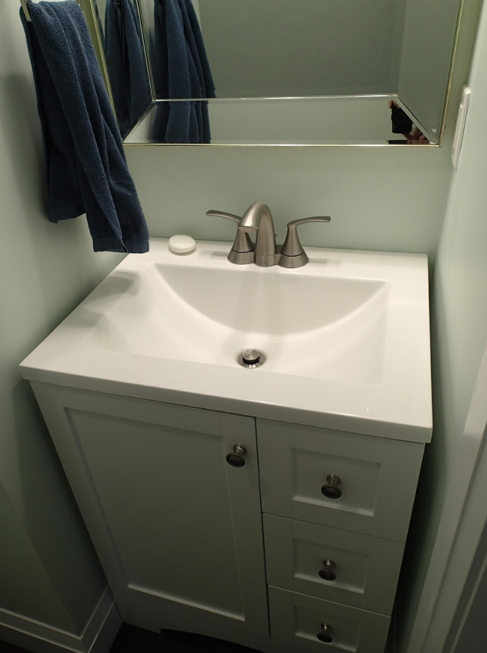 White bathroom vanity with sink, faucet, and cabinet. Blue towel hangs on a bar above.