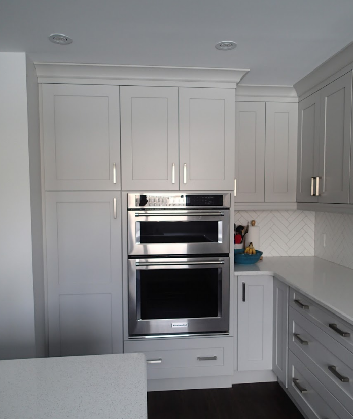 Built-in stainless steel oven and microwave in white kitchen cabinets. Counter and drawers to the right.