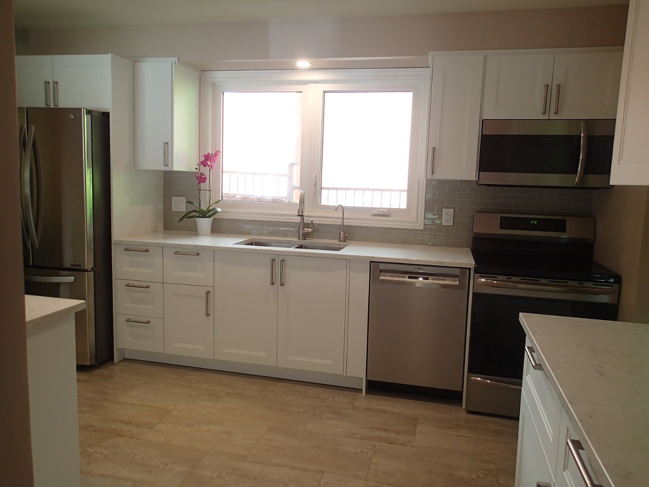 White kitchen with stainless steel appliances, window, and light-colored countertops and cabinets.