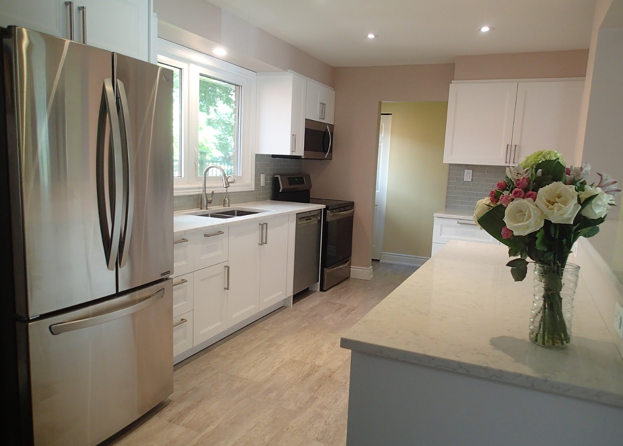 Modern white kitchen with stainless steel appliances, light countertop, and a bouquet of flowers.