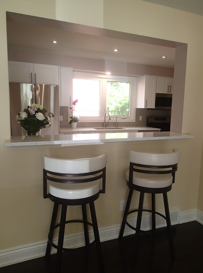 Two white and black bar stools face a pass-through to a modern kitchen.