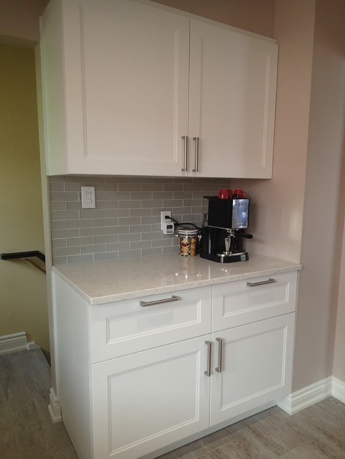 White coffee bar cabinet with a coffee maker, gray backsplash, and light countertop.