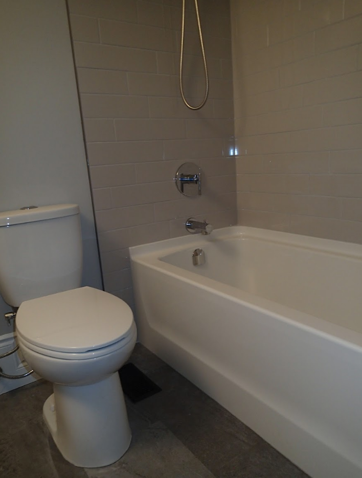 Bathroom with a white toilet and tub, gray tile wall, and silver shower head.