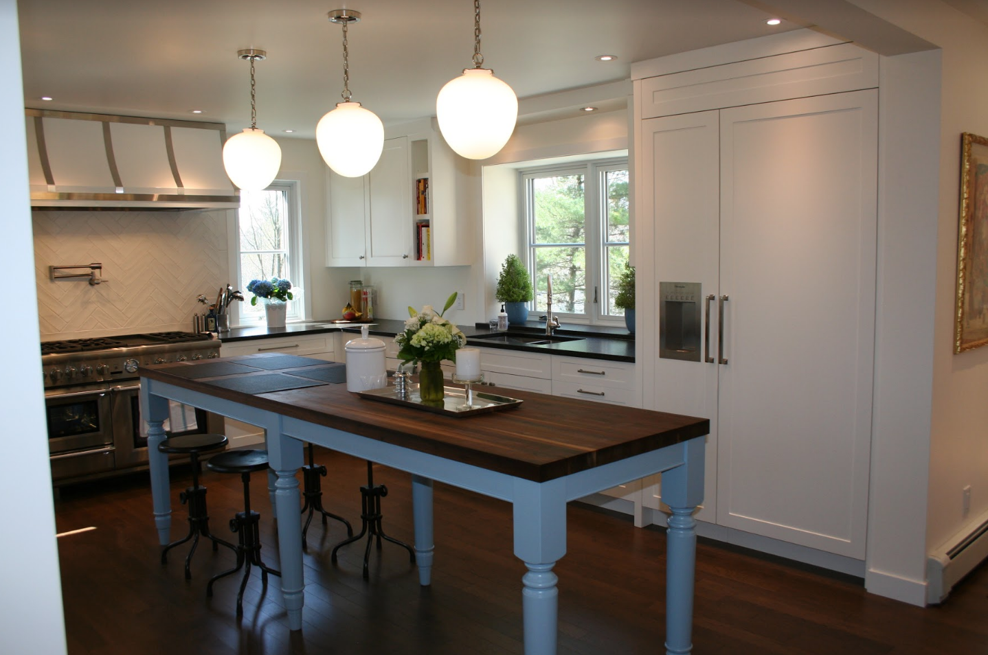 Bright white kitchen with wooden island and three pendant lights.