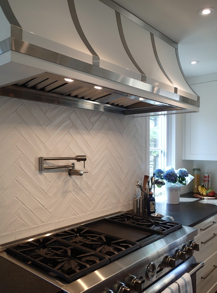 White kitchen with stainless steel appliances, herringbone backsplash, and range hood.