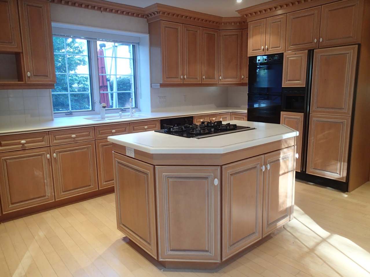 Light wood kitchen with island, stove, cabinets, and a black oven. Window in the background.