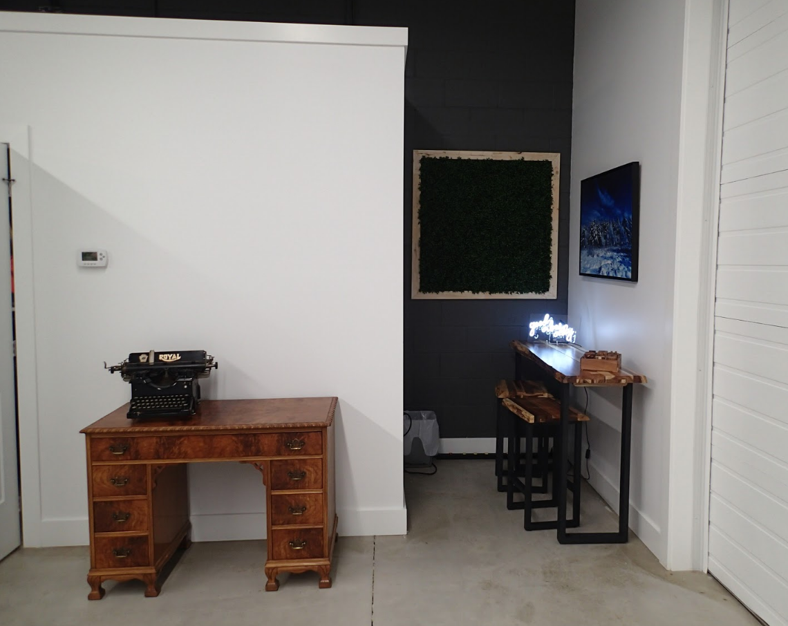 Room with desk, typewriter, and bar with stools. Green wall art, and dark wall section.