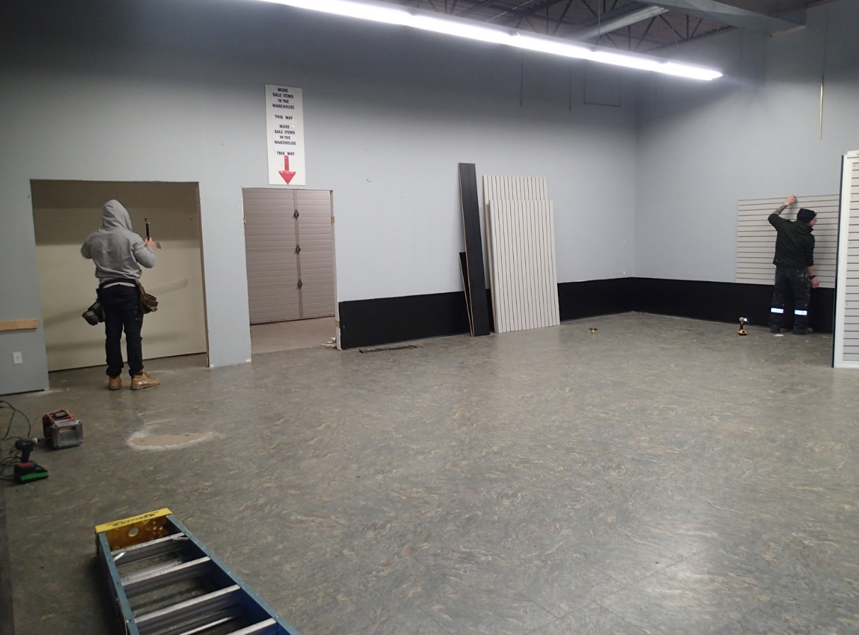 Workers renovating an interior space; gray walls, concrete floor, doorways, and materials.
