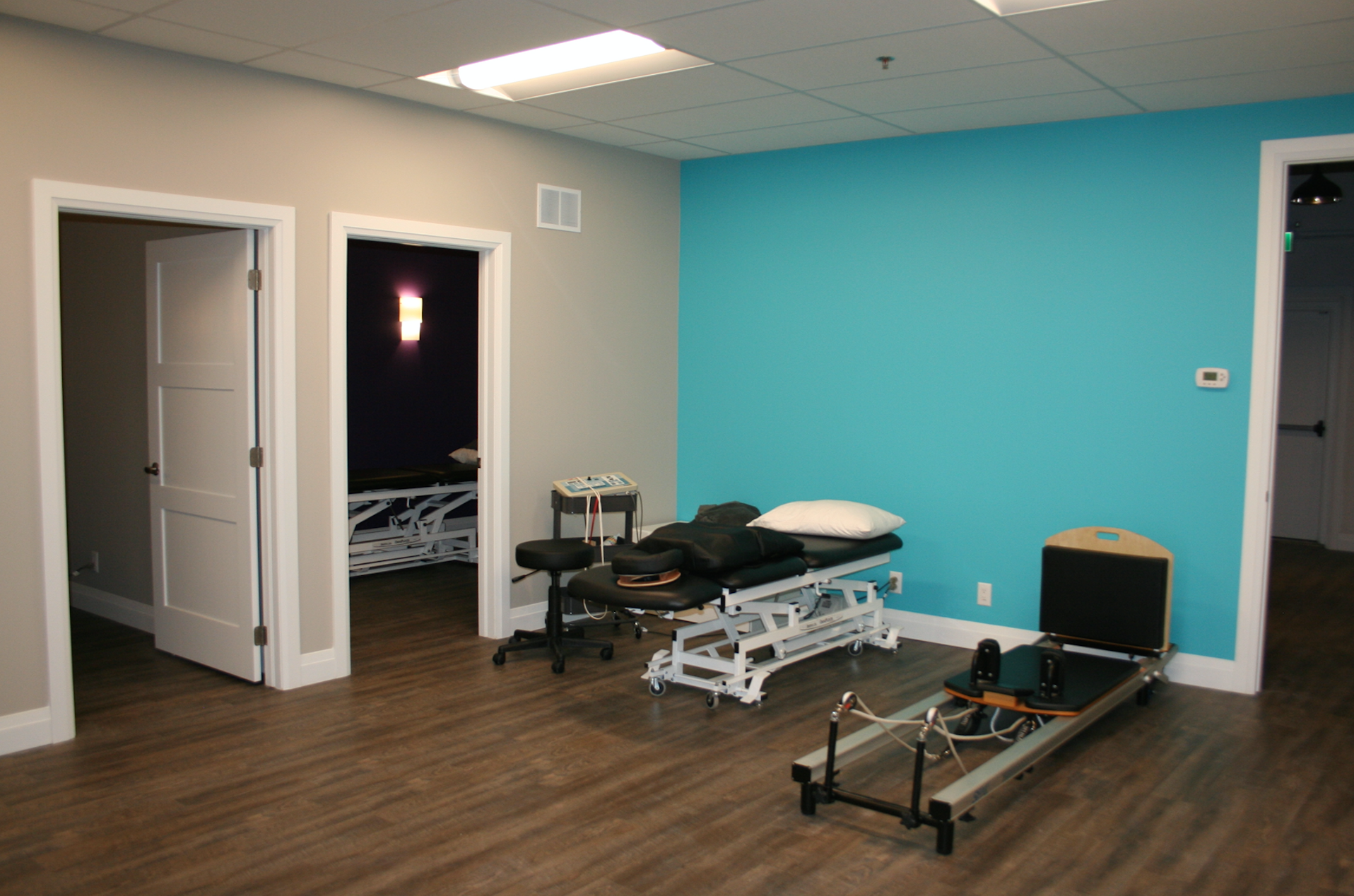 Pilates and therapy room with equipment and doors, blue and beige walls, wooden floor.