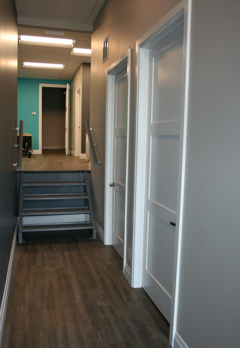 Hallway with gray walls, white doors, and a metal staircase leading to a turquoise room.