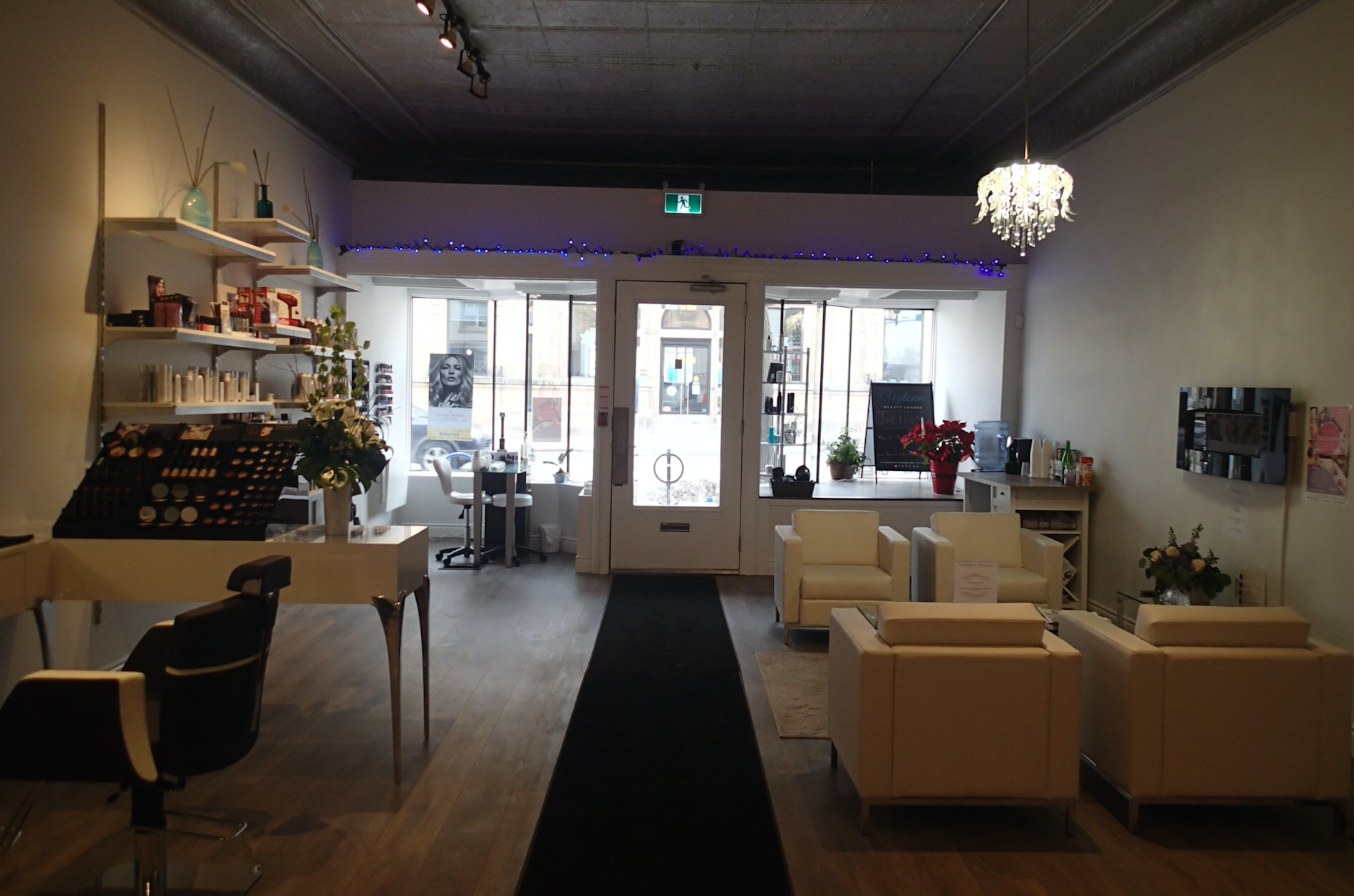 Interior of a beauty salon with white walls, seating area, and product displays. Black rug leads to entrance.