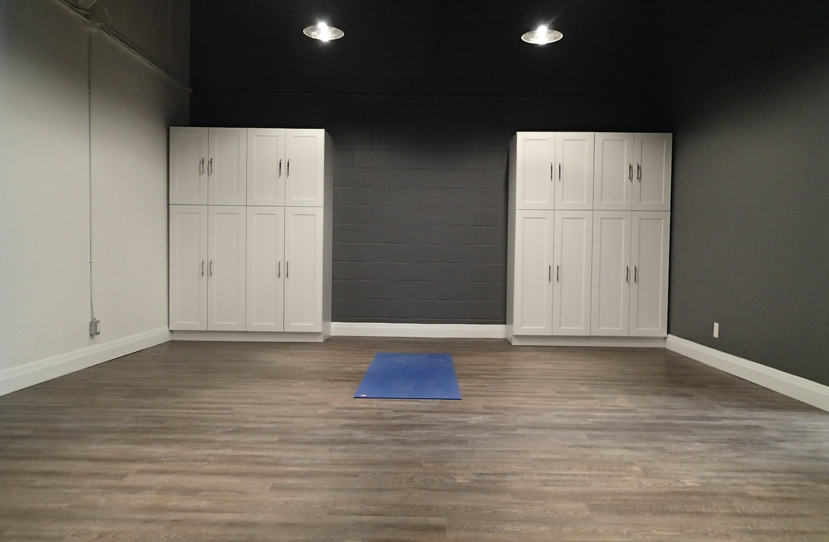 Empty room with wood floor, white cabinets, and a yoga mat. Dark gray accent wall and ceiling.