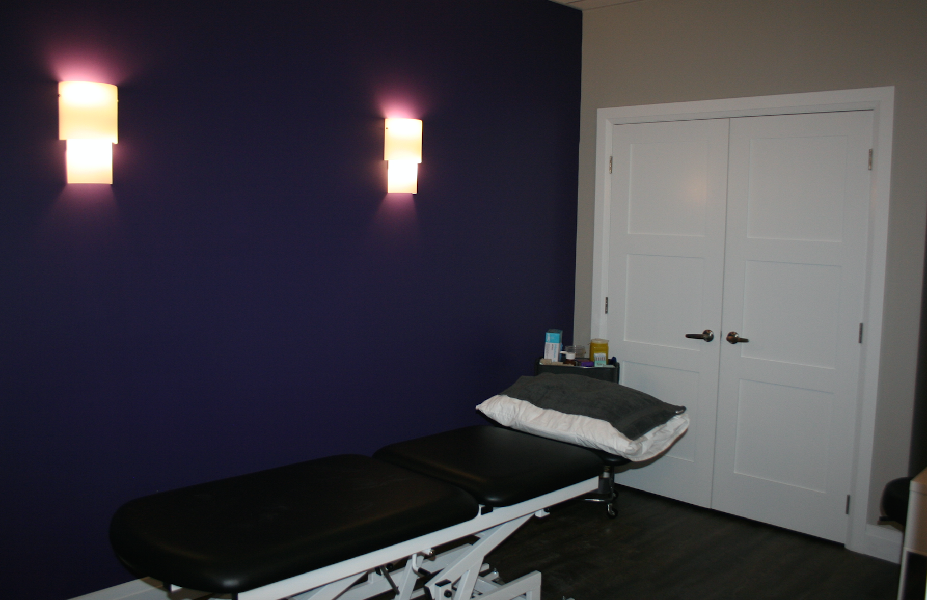 A massage table in a room with purple wall, white door, and sconce lighting.