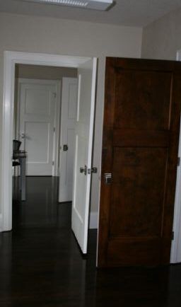 Hallway with dark wood floors, three open doors, two white and one brown, leading to other rooms.