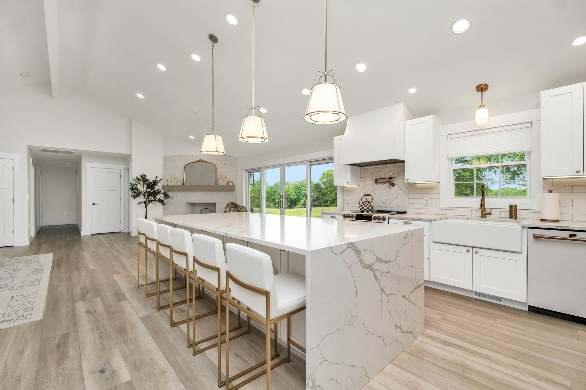 Bright white modern kitchen with island seating and a large window overlooking a green lawn.
