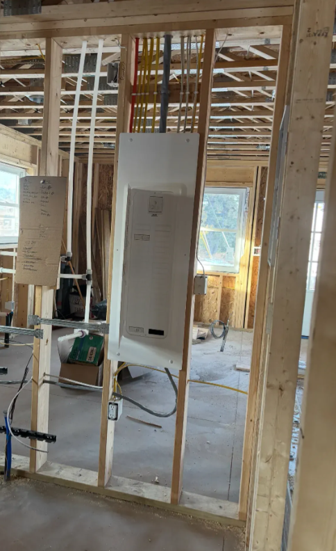 Interior framing of a house under construction with exposed studs and a white electrical panel on the wall